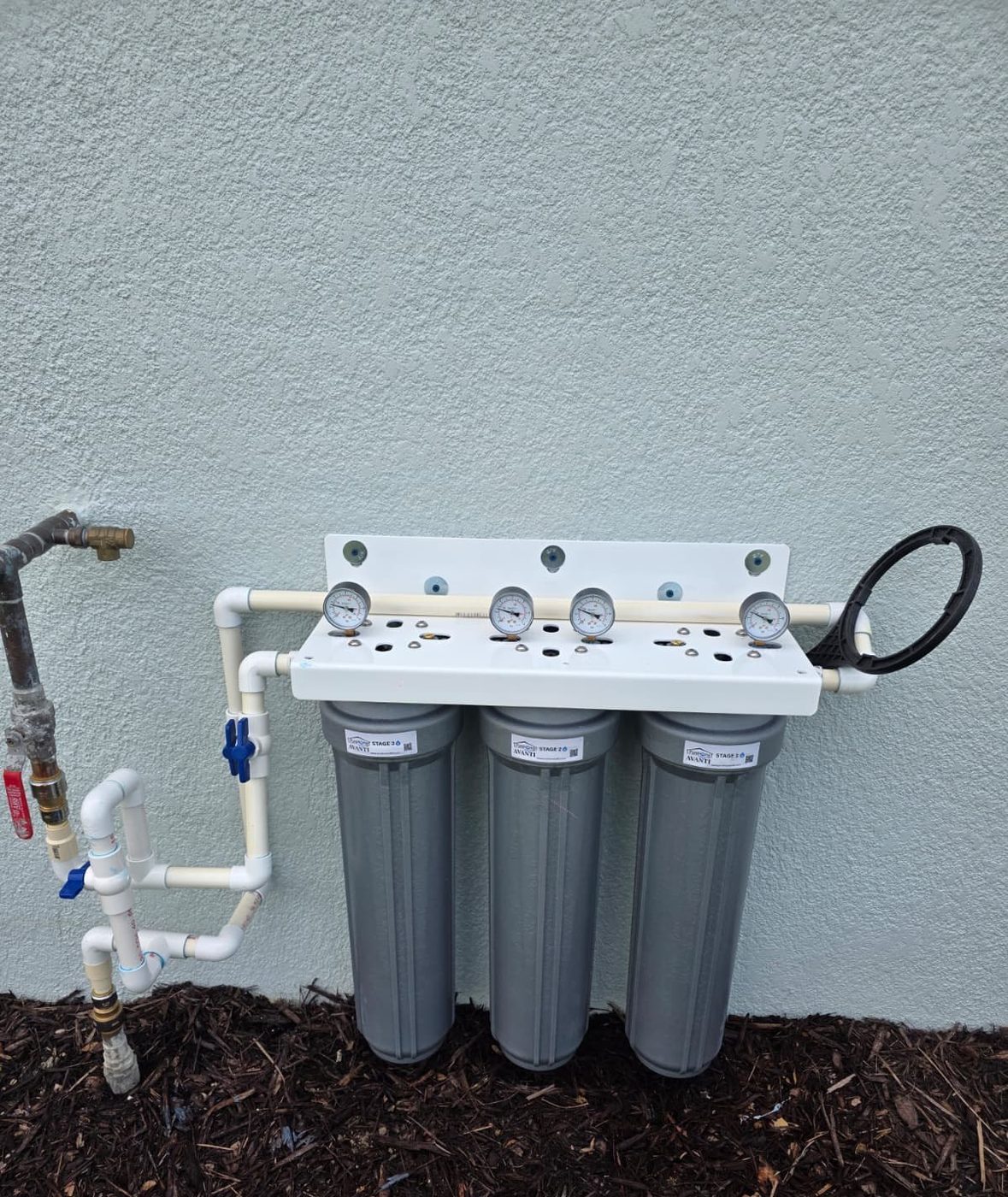 A three-stage AVANTI whole-home water filtration system plumbed into a home exterior wall