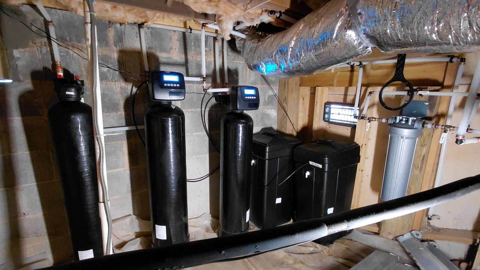 A whole-home water system in a basement: three filtration tanks with control heads, two brine tanks and a housing filter