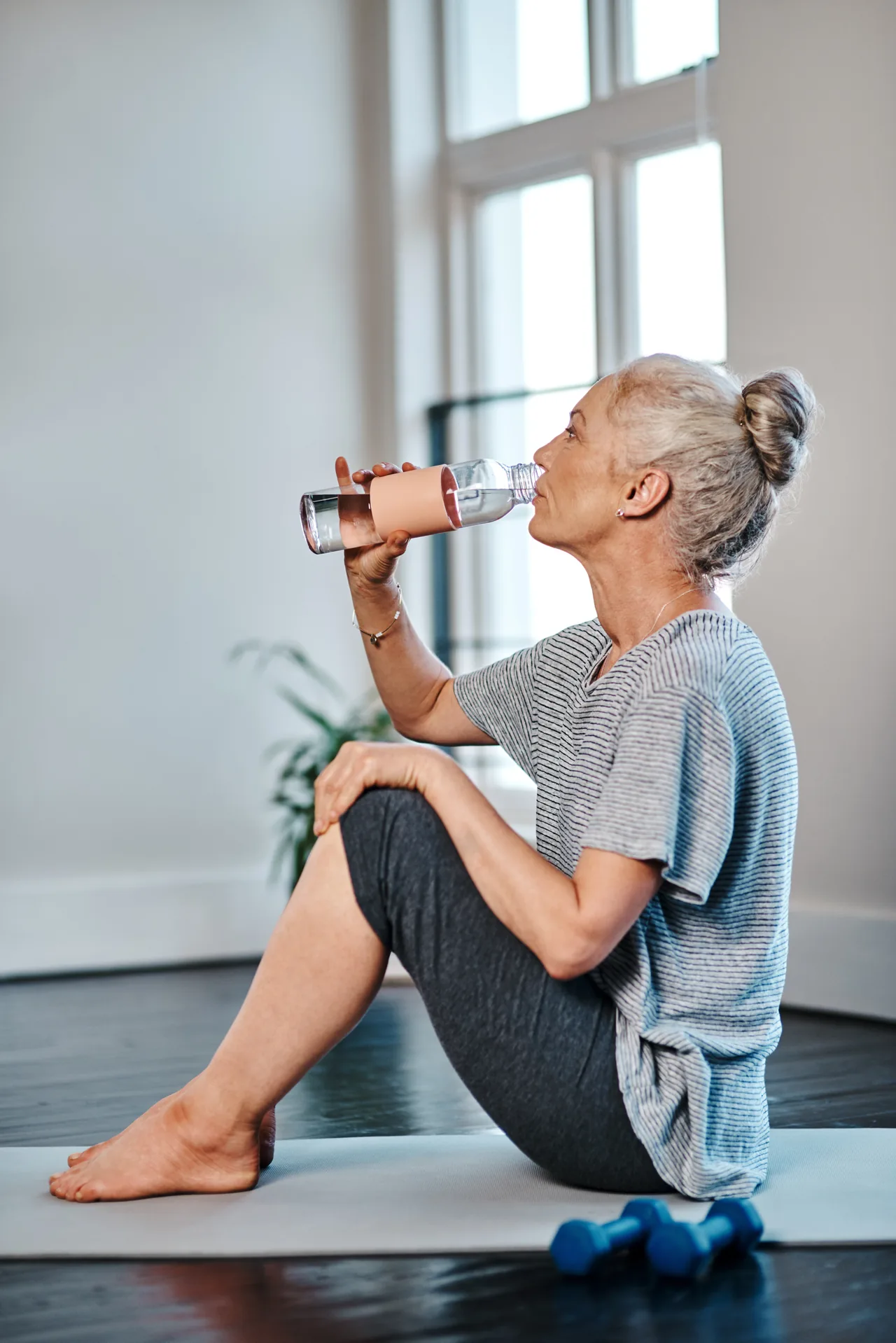 Senior woman drinking water after exercising at home