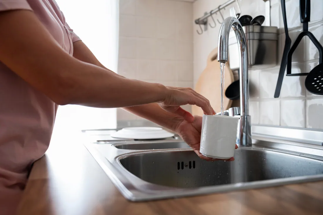 Homeowner rinsing a mug with clear water at the kitchen sink